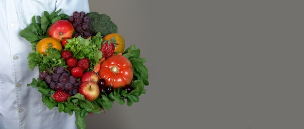 Concetto sano e nutrizione. medico che tiene una ciotola di frutta e verdura fresca su sfondo grigio.