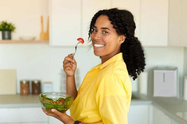 Healthy nutrition Positive african american woman eating yummy vegetable salad in kitchen at home