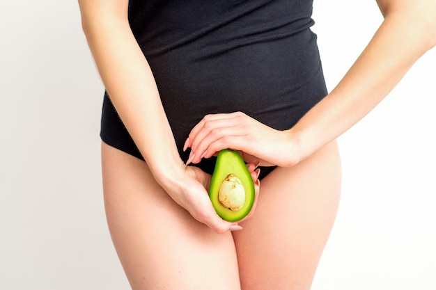 Healthy nutrition and pregnancy concept Young woman holding one half of an avocado fruit close to her belly over a white background