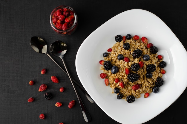 Healthy oatmeal porridge with mix of wild berries on dark background