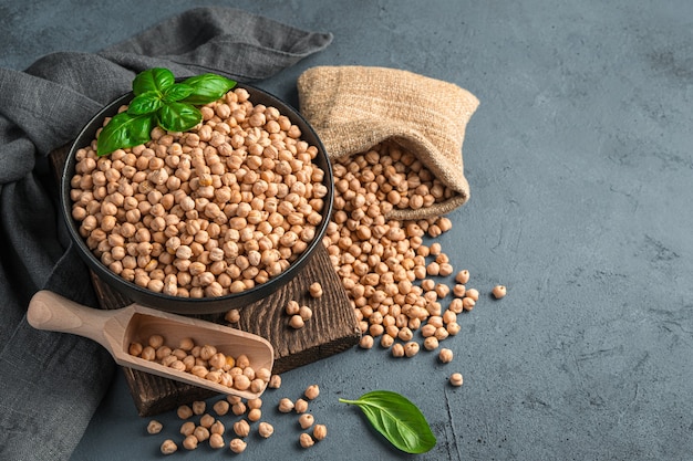 Healthy, organic chickpeas in a bowl and a linen bag on a dark background. Side view, horizontal.