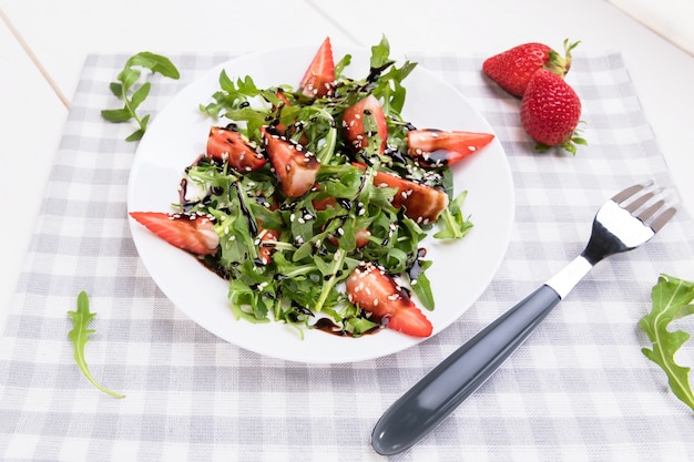 Healthy organic diet salad with arugula, strawberries and sesame with balsamic glaze