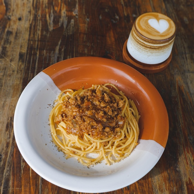 Healthy plate of Italian spaghetti topped with a tasty tomato and ground beef Bolognese sauce and fresh basil on a rustic brown wooden table Served with cappuccino