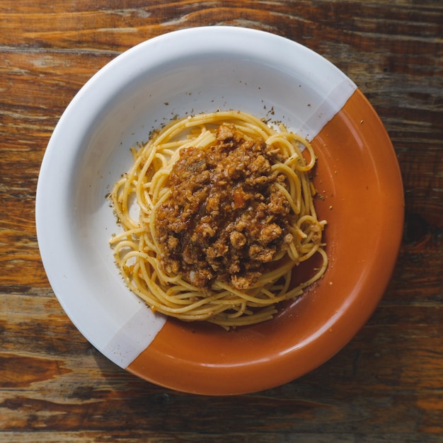 Фото Здоровая тарелка итальянских спагетти с вкусным соусом из помидоров и говяжьего фарша и свежим базиликом на деревенском коричневом деревянном столе