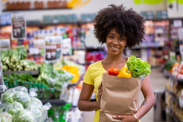 healthy positive happy african woman holding a paper shopping bag full of fruit and vegetables.