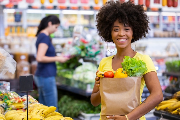healthy positive happy african woman holding a paper shopping bag full of fruit and vegetables.