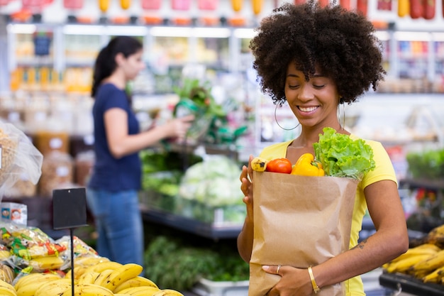 Healthy positive happy african woman holding a paper shopping bag full of fruit and vegetables.