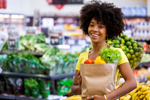 healthy positive happy african woman holding a paper shopping bag full of fruit and vegetables.