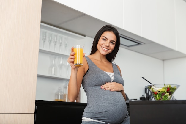 健康な妊婦が自宅の自宅のキッチンでジュースを飲んでいます。