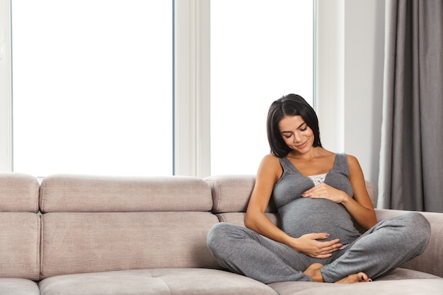 Healthy pregnant woman indoors at home sitting posing.