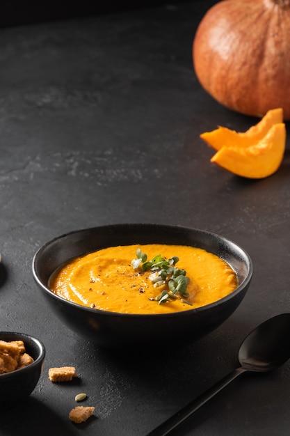 Healthy pumpkin soup garnish microgreens on black. Close up. Vertical format.