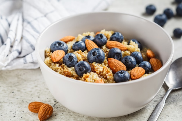 Porridge sano della quinoa con i mirtilli e le mandorle con sciroppo in una ciotola grigia. concetto di cibo vegan.