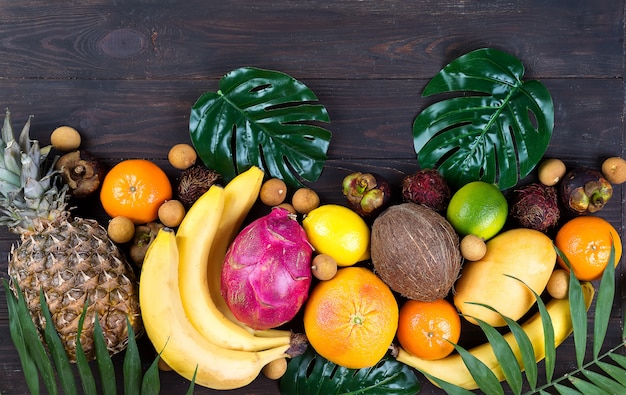 Healthy rainbow tropical fruits frame with palm leaves on blue wooden table