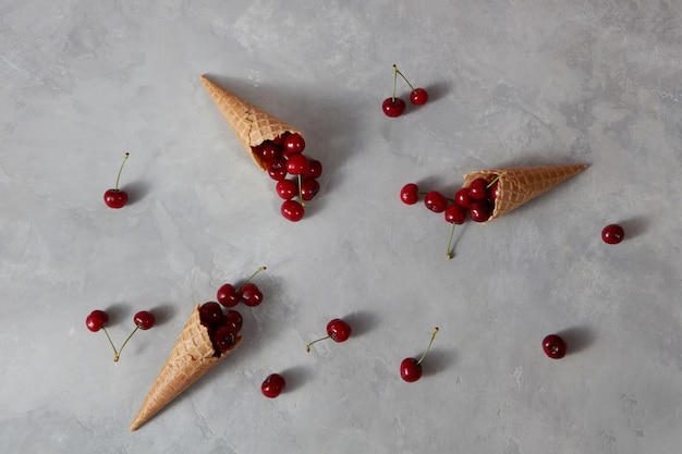 Здоровые спелые красные фрукты вишня и вафельные чашки для домашнего мороженого на сером каменном фоне с местом для текста. Летом органическое питание.