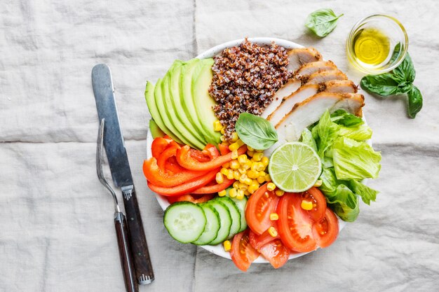 Healthy salad bowl with quinoa, tomato turkey, avocado, sweet pepper, corn, lime and mixed greens, top view. Healthy food conception. Superfood meal.