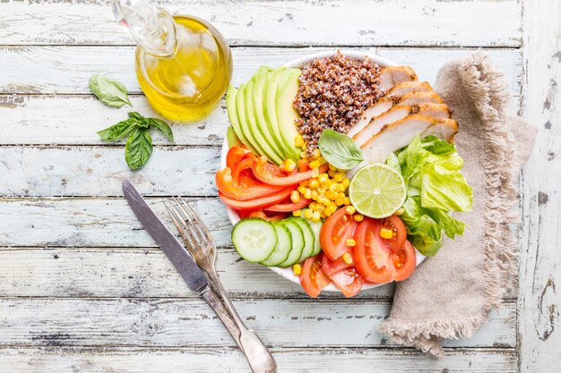 Healthy salad bowl with quinoa, tomato turkey, avocado, sweet pepper, corn, lime and mixed greens, top view. Healthy food conception. Superfood meal.