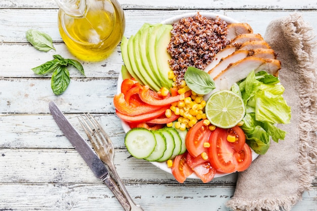 Healthy salad bowl with quinoa, tomato turkey, avocado, sweet pepper, corn, lime and mixed greens, top view. Healthy food conception. Superfood meal.