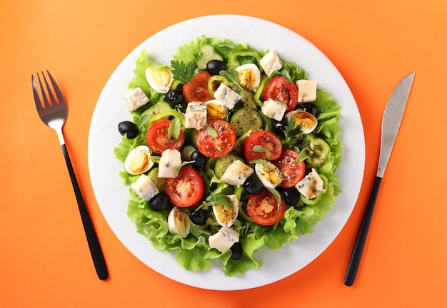 Healthy salad of cherry tomatoes, cucumbers, peppers, black olives, with olive oil, quail eggs and gorgonzolla cheese on a orange background.