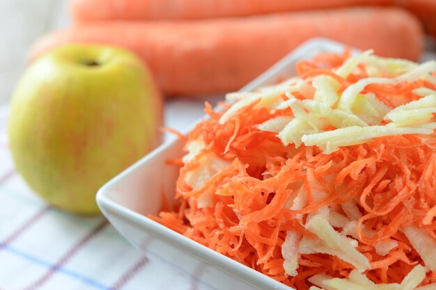 Healthy salad concept grated carrot with apple in a white platter in closeup