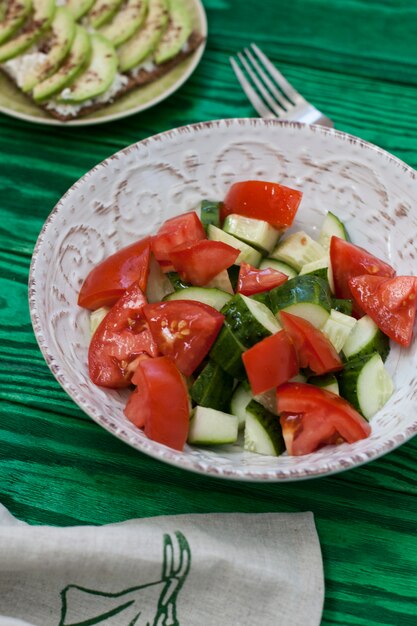 Una sana insalata di pomodori freschi e verdure e un panino fatto in casa con formaggio morbido, avocado e condimento con toast di grano duro. una colazione salutare.