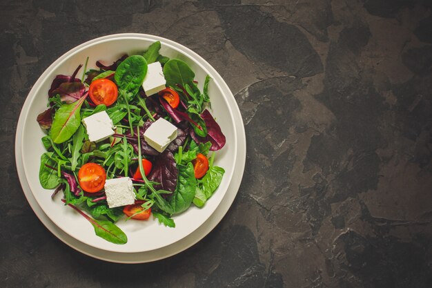 Healthy salad leaves in a white plate and cheese (mix micro greens, juicy snack). food background