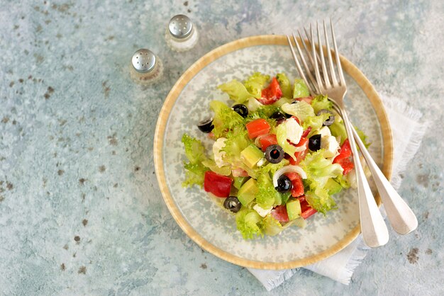 Healthy salad of lettuce, tomato, red pepper, soft cheese, olives, avocado, onion with olive oil and lemon juice.