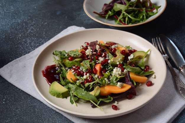 Healthy salad persimmon, blue cheese, spinach, arugula, lettuce leaves on white plate