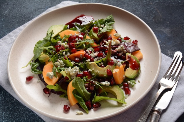 Healthy salad persimmon, blue cheese, spinach, arugula, lettuce leaves on white plate