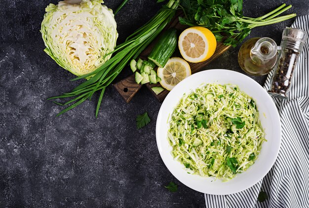 Healthy salad. Spring vegan salad with cabbage, cucumber, green onion and parsley on dark table. Top view