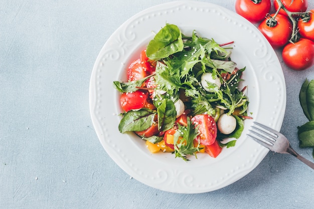 Healthy salad with cherry tomatoes, herbs and mozzarella top view.