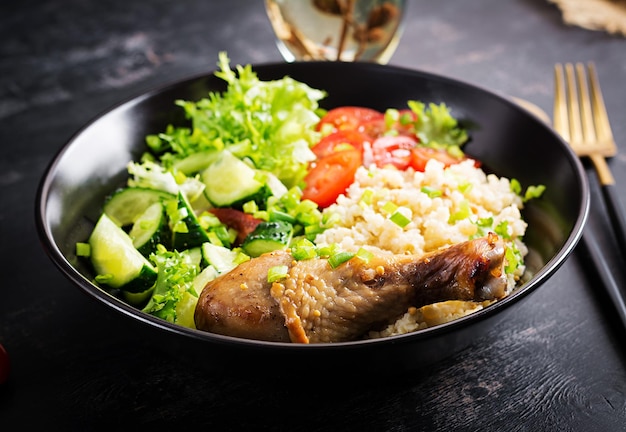 Здоровый салат с куриной ножкой, помидорами, огурцом и салатом на темном фоне. Здоровый обед. Диетическое меню.