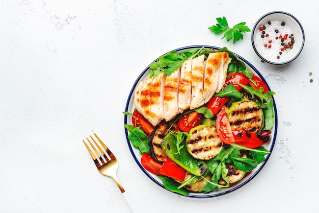 Healthy salad with grilled chicken breast fillet and vegetables paprika zucchini eggplant fresh tomatoes and mixed herbs White table background top view