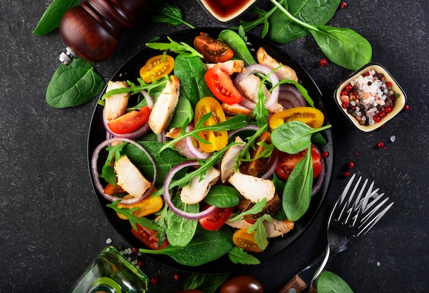 Healthy salad with spinach grilled chicken tomatoes arugula and red onion Black table copy space