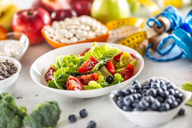 Healthy salad with tomatoes olives and olive oil surrounded by healthy food and exercise equipment