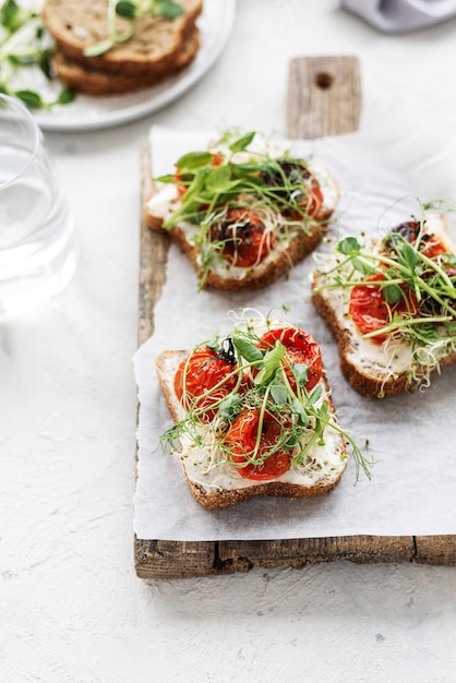 Healthy sandwich with cream cheese baked tomatoes and micro greens on white background