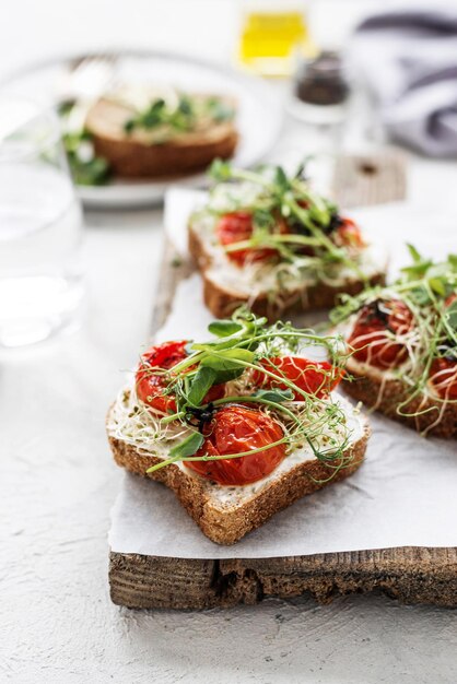 Healthy sandwich with cream cheese baked tomatoes and micro greens on white background