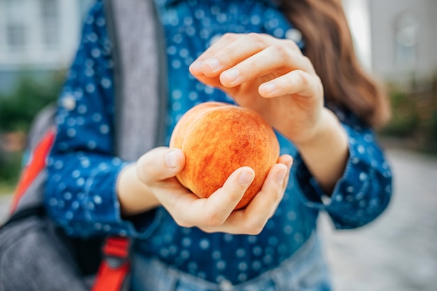 Healthy school breakfast, peach in the hands of a schoolgirl.