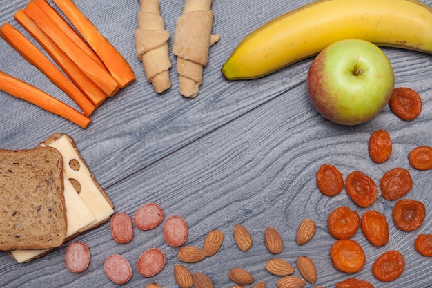 Foto sano pranzo scolastico con sandwich con formaggio, mela, banana, mandorle, frutta secca, acqua, caramelle naturali, carota, biscotti copia spazio, piatto, vista dall'alto.