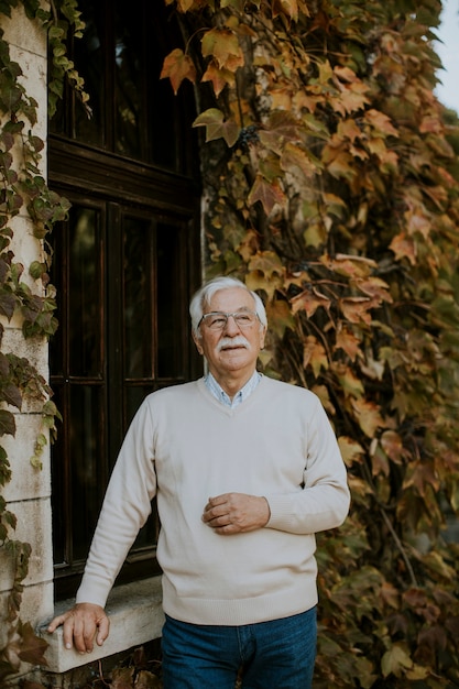 Healthy senior man standing by the window at the autumn day