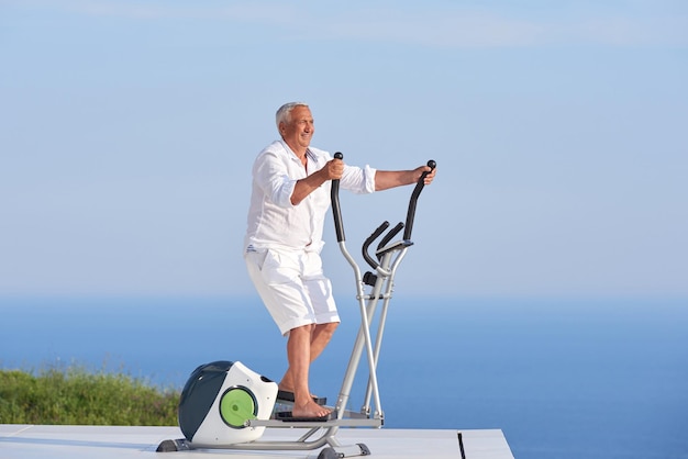 바다 전망을 감상할 수 있는 현대적인 홈 테라스에서 체육관 러닝머신에서 운동하는 건강한 노인