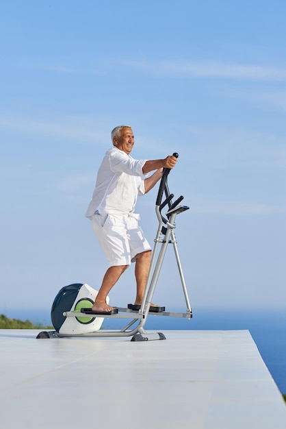 healthy senior man working out on gym treadmill machine at modern home terace with ocean view