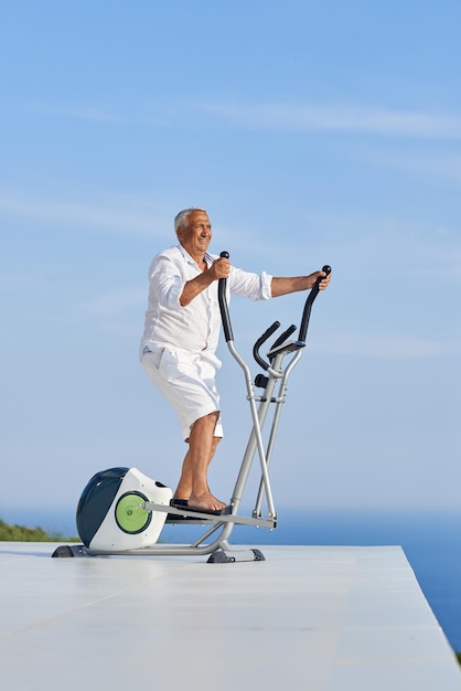 healthy senior man working out on gym treadmill machine at modern home terace with ocean view