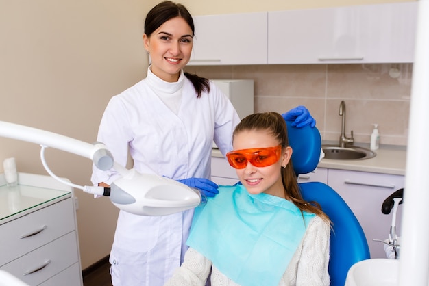 Healthy smile and healthy teeth. dentist fixes the dental filling UV lamp while the patient is sitting in dental chair and smiling broadly.