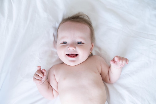 Healthy smiling baby lies on his back on bed on white bedding top view