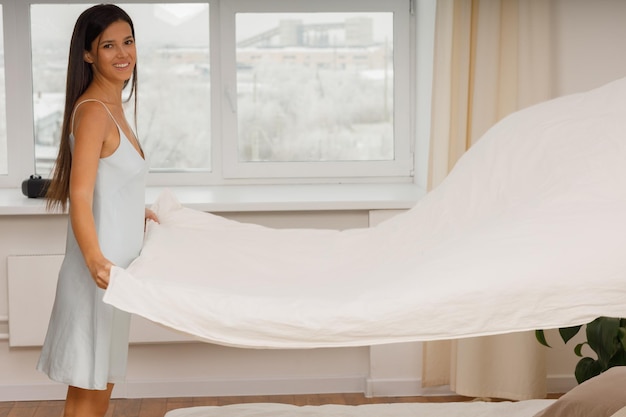 Healthy smiling young woman dressing nightie covers blanket on bed in bedroom