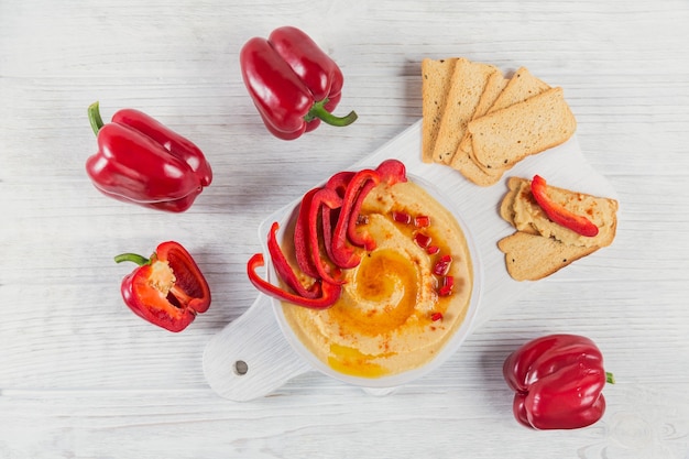 Healthy snack from crisp bread with hummus, olive oil and paprika on white wooden surface.