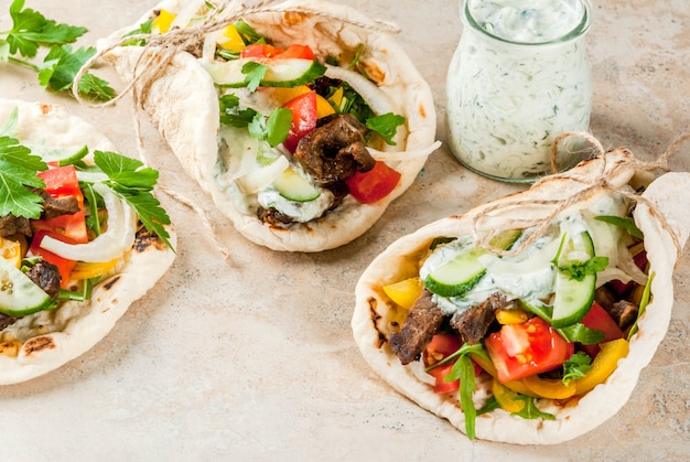 Foto spuntino salutare, pranzo. gyros sandwich tradizionali greci avvolti - tortillas, pita di pane con ripieno di verdure, carne di manzo e salsa tzatziki