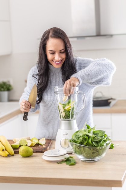 Healthy snack preparation by adding fruits and green leaves into a kitchen blender.