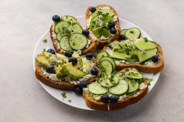 Photo healthy snack vegetarian sandwiches with vegetable cheese cucumbers and avocados on a white plate on a light background