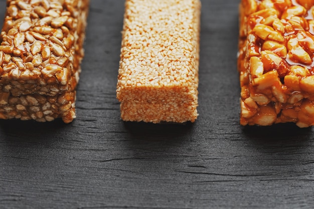 Photo healthy snacks. fitness diet food. grain bar with peanuts, sesame and seeds on a cutting board on a dark table, energy bars